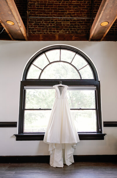 Wedding dress hanging gracefully by window in Wilmington bridal suite, capturing pre-ceremony details