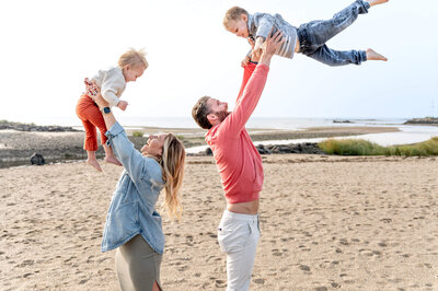 Parents throwing their two kids in the air as they stand back to back at Compo Beach in Westport, CT.
