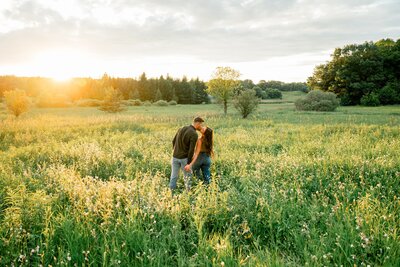 a couple walking through a grassy field kissing one another 