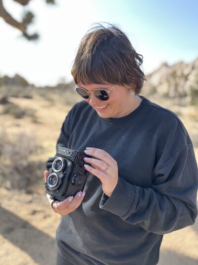 Photographer standing in golden hour light among Joshua Tree boulders, holding a medium format camera