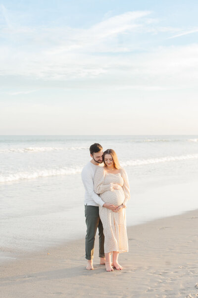 Expectant couple standing near the shoreline holding mamas belly