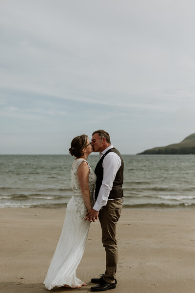 groom kissing bride on beach