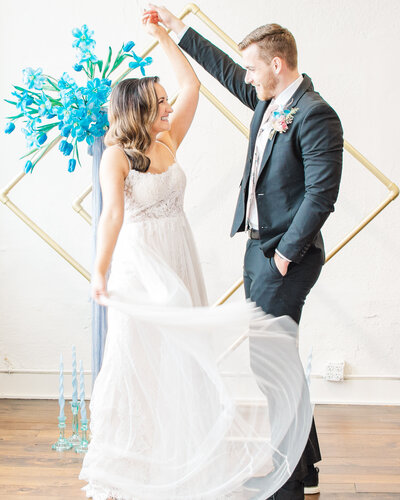 Bride is twirling her dress in front of a colorful wedding arch at the Schoolhouse Wedding Venue in Dallas Fort Worth. Taken by Danni Lea Photography, DFW Wedding Photographer