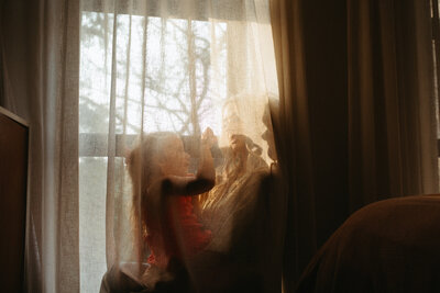 a mother and child are playing behind a curtain in a natural candid documentary moment. The photograpoh shows intimacy of motherhood 