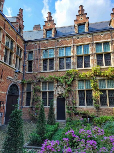Historic brick courtyard of the Plantin-Moretus Museum, featuring vine-covered walls, gabled rooftops, and blooming flowers in Antwerp, Belgium ©Stephanie Dosch | theViatrix Luxury Travel