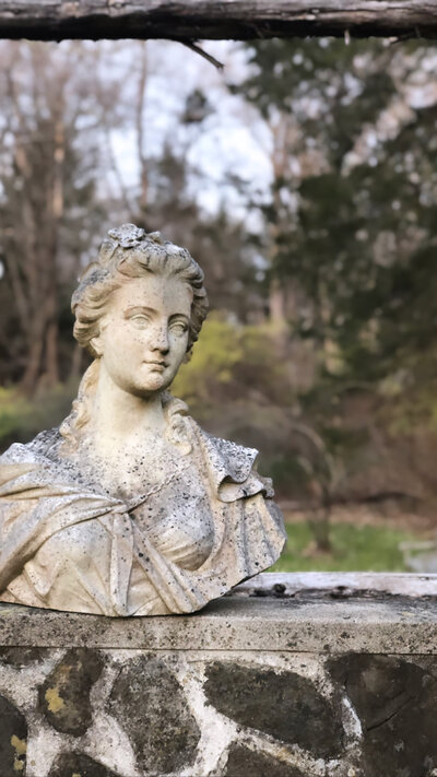 A bust of a lady sitting on a garden wall.