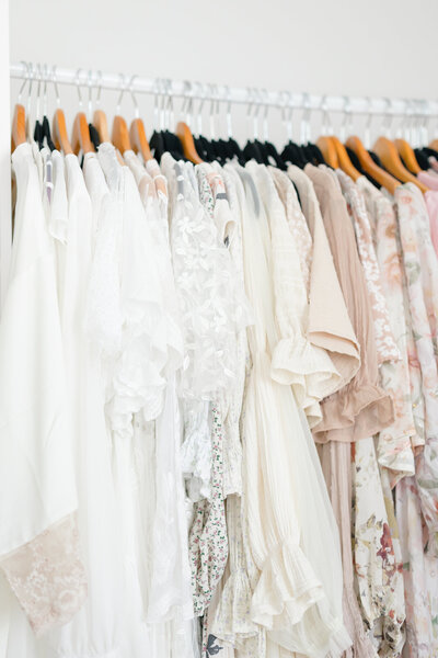 A row of beautiful light colored dresses hanging on a rack in front of a window