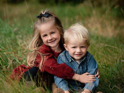 Siblings girl and boy hugging in outdoor grass setting