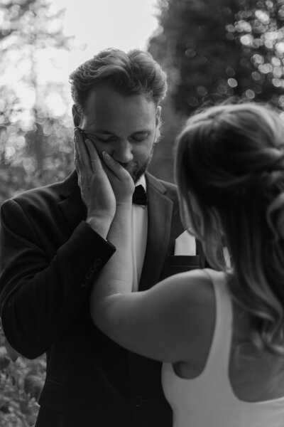 Bride holding the groom's cheek in her palm, the groom placing her hand on her hand, in black and white.