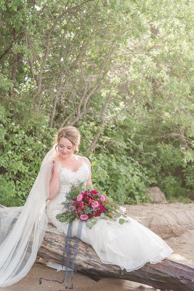 bride holding a bouquet sitting on a fallen tree