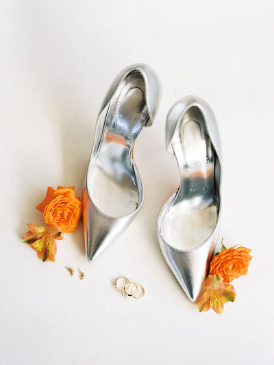 Silver wedding shoes on a white background with orange flowers and wedding rings