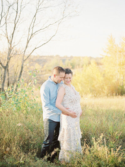 Mom and dad snuggling bump on beautiful fall day in Edmonton