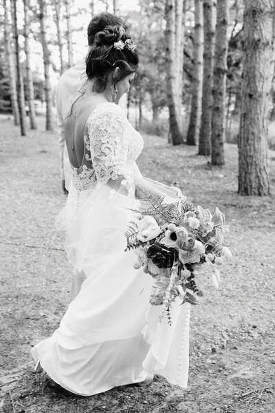Bride walking through the woods wearing her wedding dress and holding a bouquet 