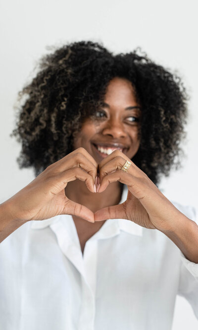 A woman crafts a heart shape, her gesture conveying warmth and affection