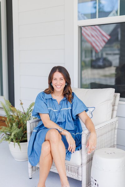 Woman sitting on a porch chair smiling at the camera.