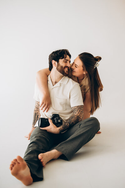 A person sitting on their floor with their partner leaning over their shoulder about to kiss