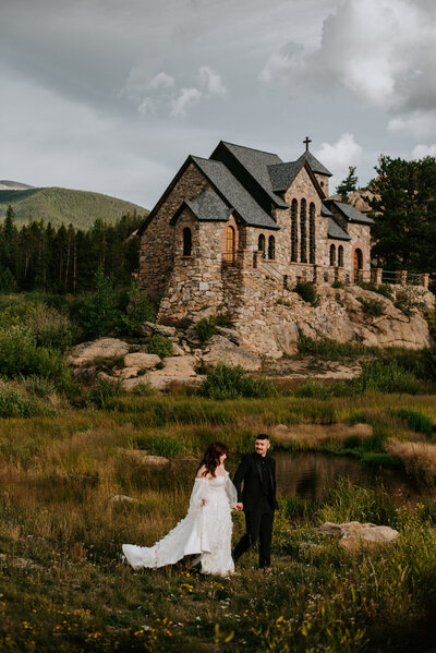 A couple walking through flower and tall grass in front of a beautiful chapel in Estes Park, Colorado