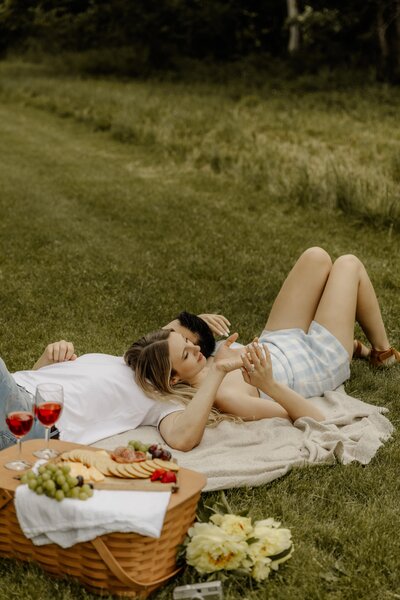 A couple in love lie next to each other on a  picnic blanket with intertwined hands.