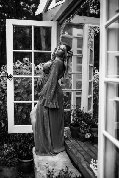 Black and white image of a pregnant woman posing near french doors