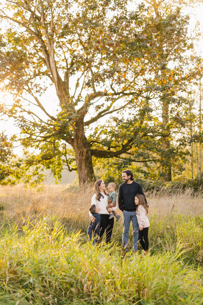 Photo of a family of five in a grassy field in front of a big tree