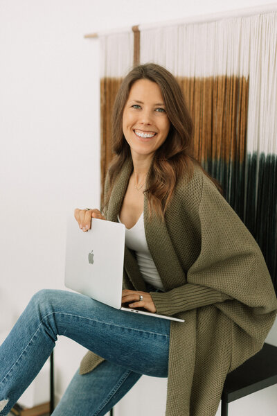 A  portrait  of luxury copywriter and brand messaging expert Sydney, owner of Back Label Branding. Sydney is looking at the camera and smiling, while holding her laptop computer. Photo used to accompany her honest review of Foxtail Tech.