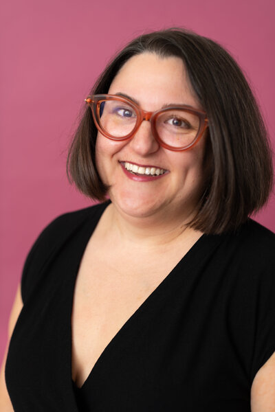 Headshot of Founder Sydney in black shirt with pink background