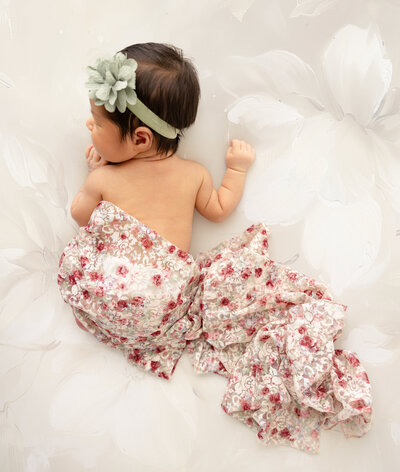 8 day newborn girl lying on stomach, wearing a green bow headband and a lace wrap covering her bottom.