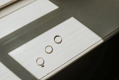 wedding rings on a window sill with the shadows of the window