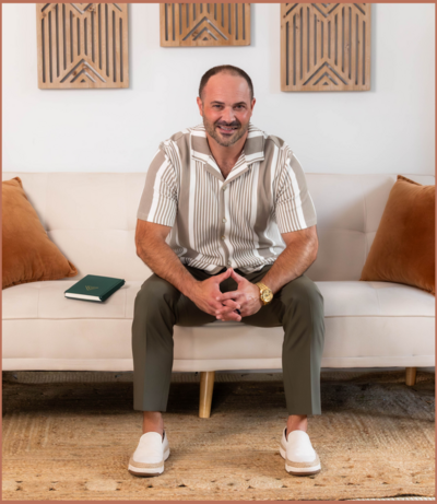 man sitting on a couch with hands together smiling at the camera