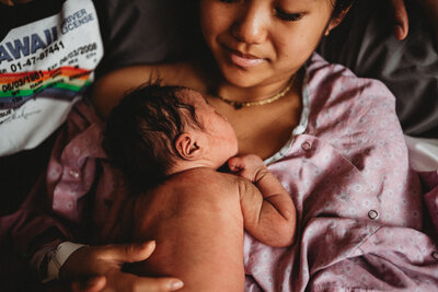 Twin Cities Fresh 48 image of new mom in the hospital in a hospital gown holding her newborn baby girl on her chest
