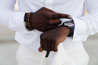 Close-up of man’s wrist with a watch and beaded bracelets, adjusting his sleeve