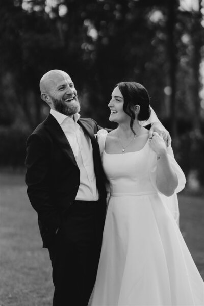 Bride and groom laughing together outdoors in a candid, documentary-style wedding photo.
