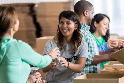 Smiling woman in a 'volunteer' shirt greeting others in a community setting.