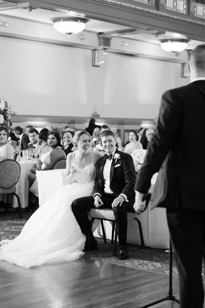 black and white candid image of bride and groom laughing at a toast during their Hotel John Marshall wedding reception