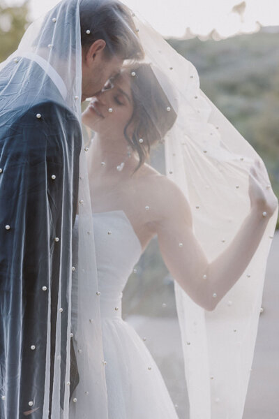 Bride and groom under pearl veil, backlit from the sun.  elegant editorial intimate wedding at monserate. southern california wedding