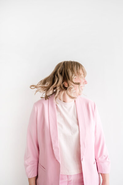 Kat Murphy in a light pink blazer shaking her hair in front of a white background