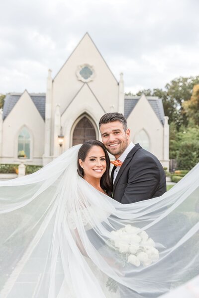 Bride and groom in front of church with veil in front