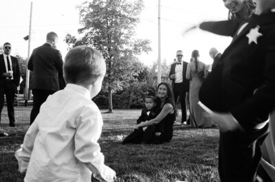 A mother sits on the ground with a child, while friends and family mingle around