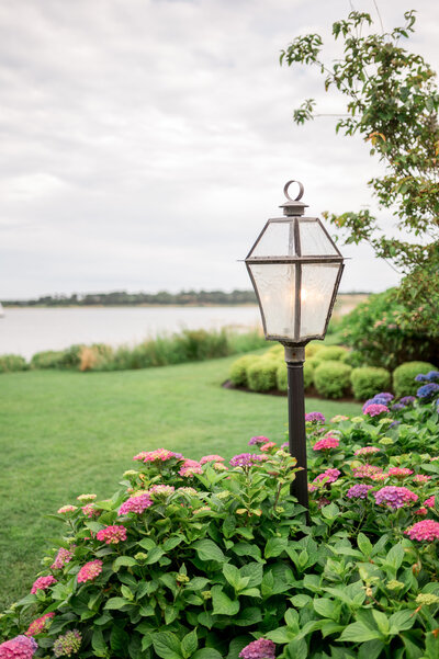 A black lantern-style lamp surrounded by blooming pink and purple hydrangeas on a lush green lawn overlooking the water at Wequassett Resort's ceremony spot.