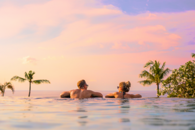 couple relaxes over the edge of an infinity pool watching the sunset