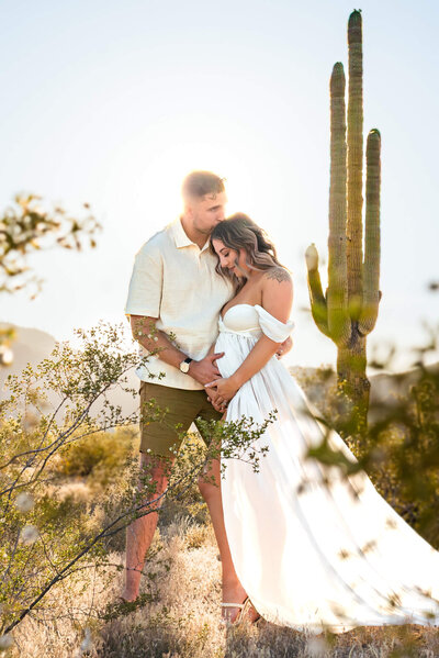 Breathtaking photograph of expecting parents hugging near cacti. Captured by Cactus & Pine Photography