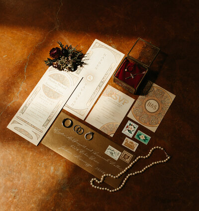 Wedding invitations laying on floor with rings and boutonniere