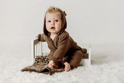 six month old baby boy sitting in brown knit bear outfit for his Colorado Milestone session