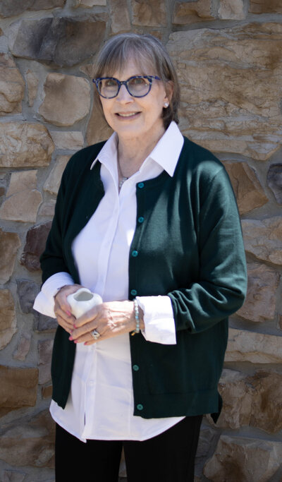 Carolee Frye posing for a headshot behind a rustic stone wall. 