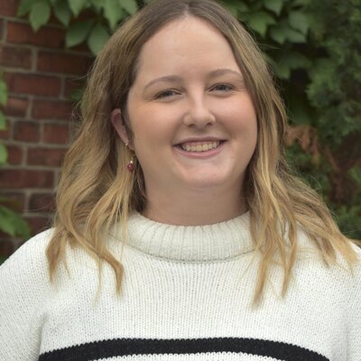Jessica wearing a white blazer, smiling as she writes in her planner