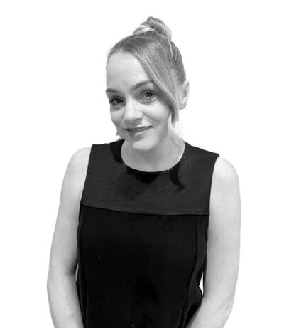 Advanced Senior Stylist with long wavy hair in a sleeveless black dress, specializing in modern hair styling techniques.