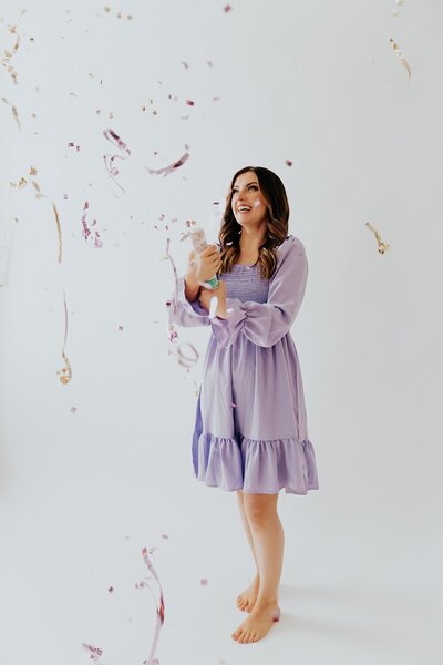 Caitlin wearing a lavender dress and popping a confetti popper