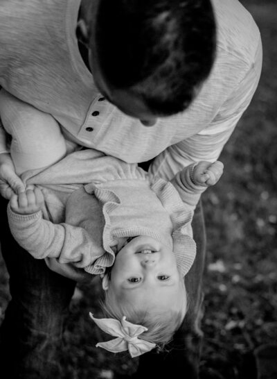 Black and white photo of dad playing with baby daughter by leaning forward with her in Annapolis Maryland