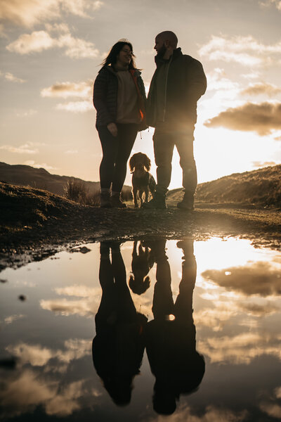 Wedding photo and video duo with their dog at sunset in the Lake District, reflected in a puddle.