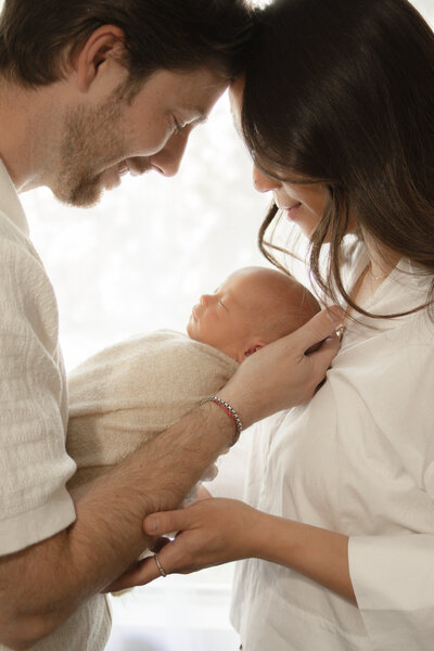 mom and dad facing each other with foreheads touching while dad holds newborn son in between them